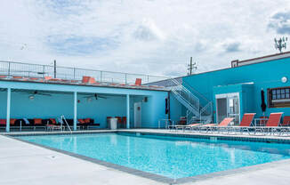 A swimming pool with red lounge chairs and a blue building in the background.