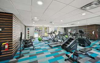 Fitness room in Amber Grove Apartments featuring treadmills, ellipticals, and weight machines