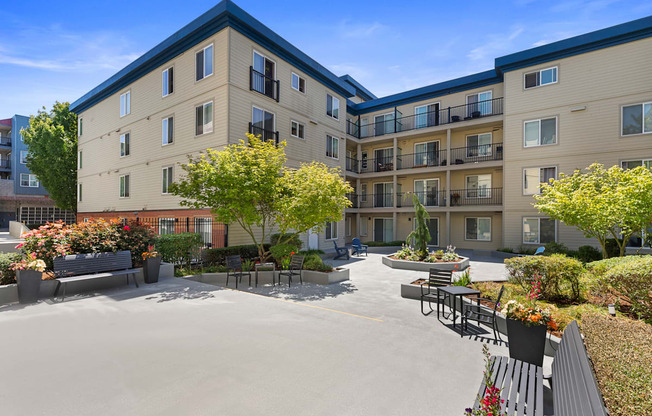 a courtyard with a paved lounge area and benches with landscaped trees and bushes at Guinevere Apartment Homes, Seattle, WA