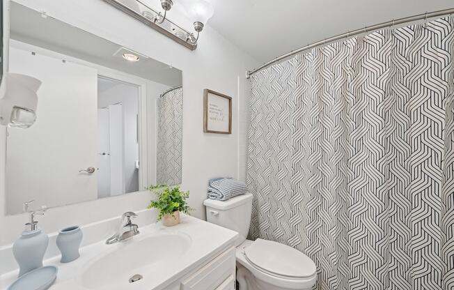 A bathroom with a white sink, toilet, and a grey and white shower curtain.