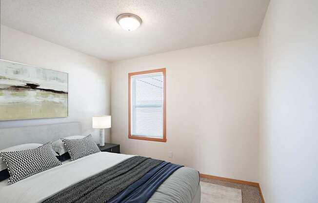 A bedroom with a bed, pillows, a lamp, and a painting on the wall. West Fargo, ND Sheyenne Terrace Townhomes