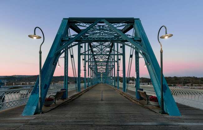 a bridge over the water at sunset with benches on it at District at Riverside Apartments, Tennessee, 37406