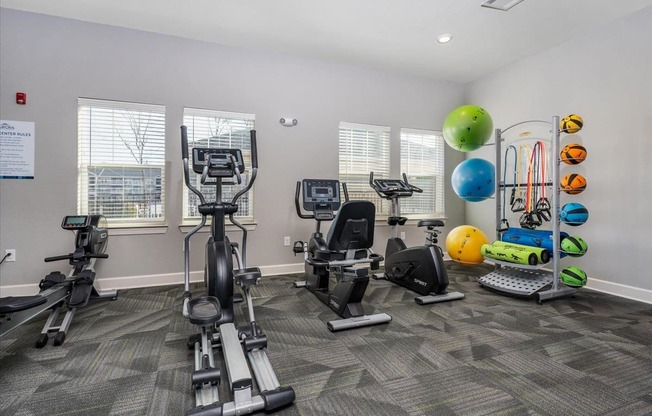 a gym with cardio equipment and weights in a room with windows