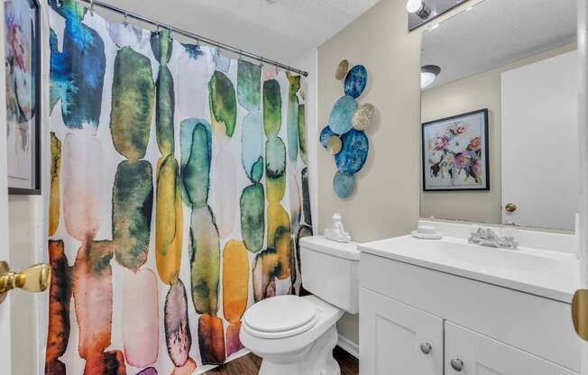A bathroom with a white toilet and a shower curtain with a watercolor design.