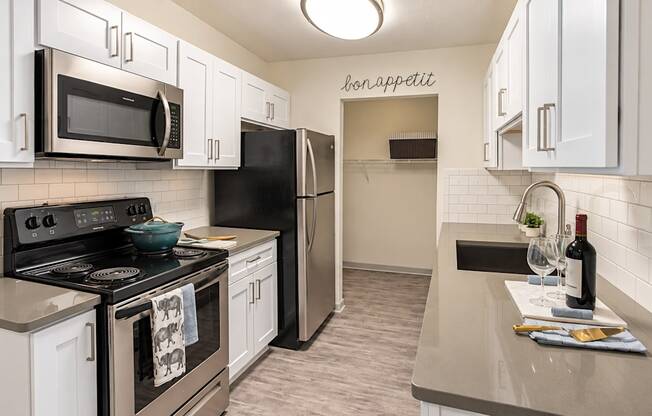 Galley kitchen with white cabinets, gray countertops, subway tile and stainless steel appliances at Icon Avondale Apartments in Decatur, GA.