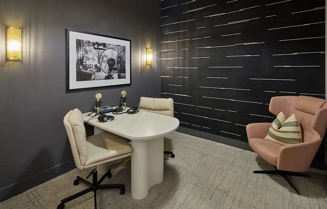 A black and white picture hangs on a dark wall above a white table with a laptop and a chair with a striped pillow on it.