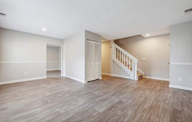 A spacious room with wooden flooring and a staircase.