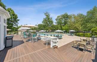 A wooden deck with chairs and umbrellas overlooking a pool.