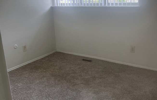 The bedroom in a 1 bedroom unit with a large window and gray carpet.