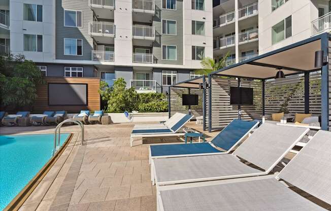 A pool area with sun loungers and a building in the background.