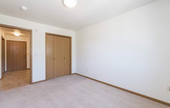 Empty living room with white walls and a door to a bedroom at Sunset Ridge Apartments in Bismarck, 58503 ND