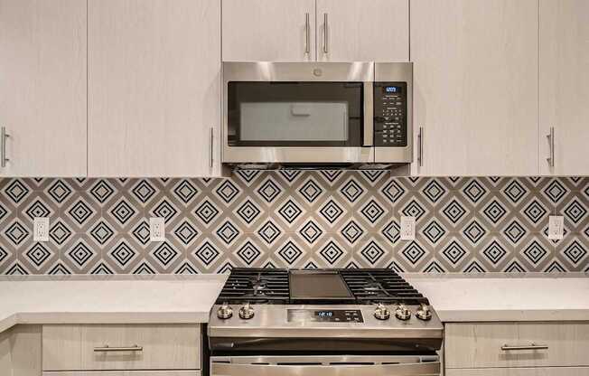 A modern kitchen with a stove, microwave, and patterned backsplash.