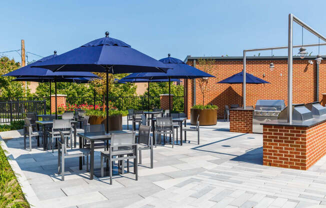 a patio with blue umbrellas and tables with chairs at One Ten Apartments, New Jersey