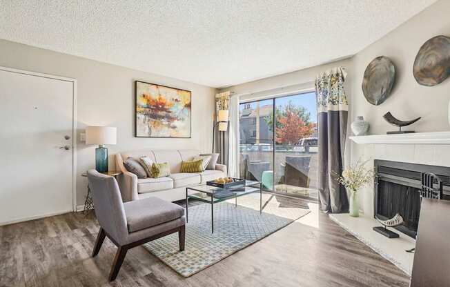 A living room with a grey armchair, a white sofa, a glass coffee table, and a fireplace.