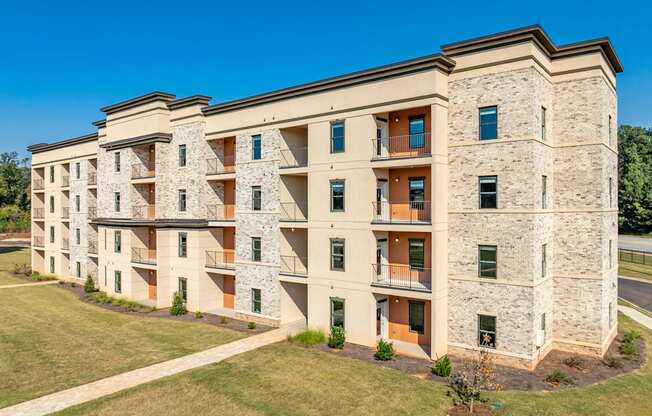 a large apartment building with brick and stone facade and a lawn