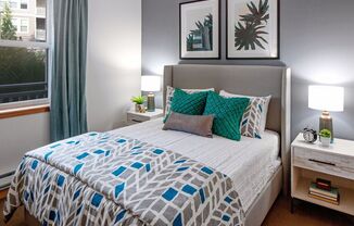A bed with a blue and white patterned comforter and two green pillows.