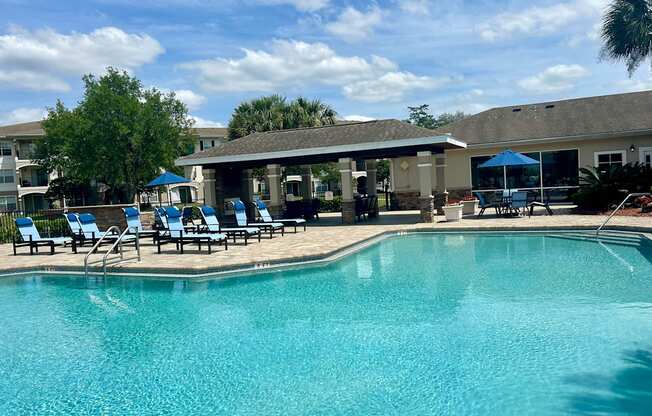 A swimming pool with sun loungers and a building in the background.