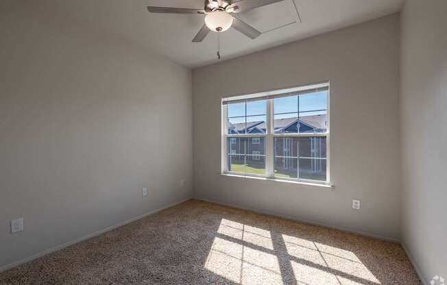 A room with a ceiling fan and a window overlooking a fenced area.