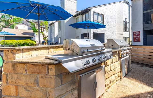 an outdoor kitchen with a grill and umbrellas at  The Beckham Apartments