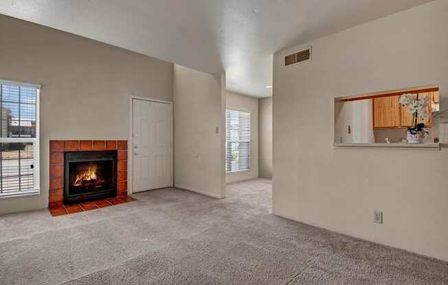 A spacious living room here at High Plains with plush beige carpet, neutral walls, and a cozy fireplace with a tiled surround, complemented by natural light from multiple windows and a pass-through opening to the kitchen for a warm, open feel.