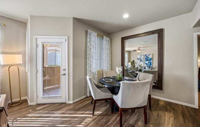 A dining room with a table set for two and a view of a door with blinds.