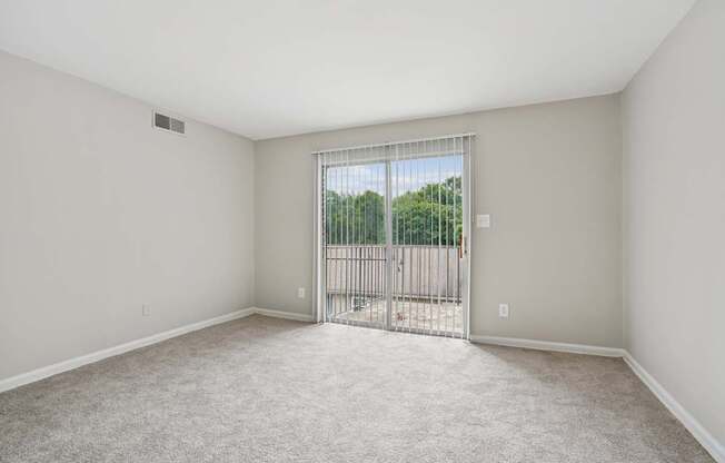 A room with a carpeted floor and a sliding glass door leading to a balcony.