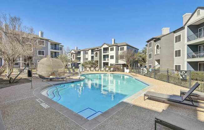 A pool surrounded by apartment buildings and a sun lounger.