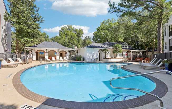A large outdoor swimming pool surrounded by trees and lounge chairs.