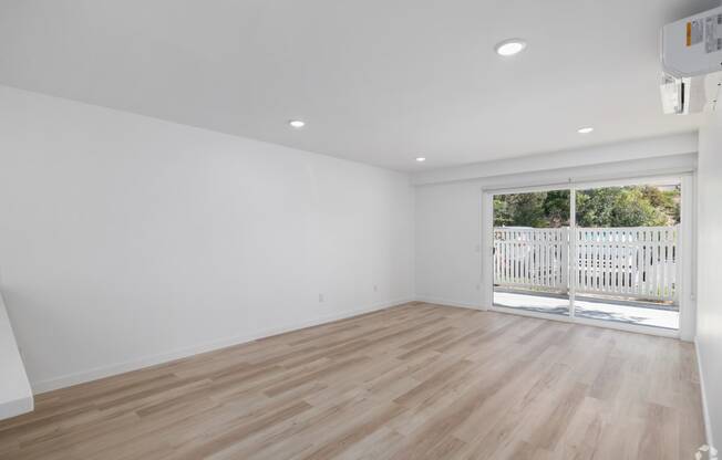 a living room with white walls and a sliding glass door to a balcony