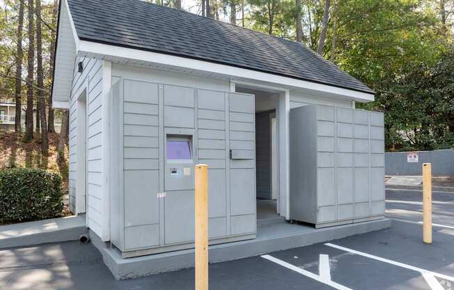 A small white building with a black roof is situated in a parking lot.