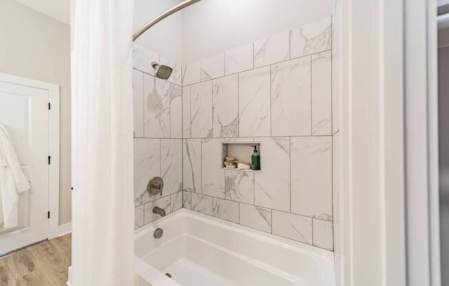 A white bathroom with a marble tile wall and a white tub.
