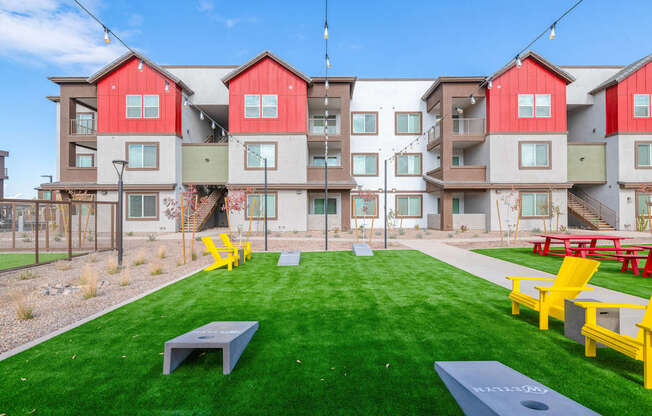 A grassy area in front of apartment buildings with yellow chairs and tables.