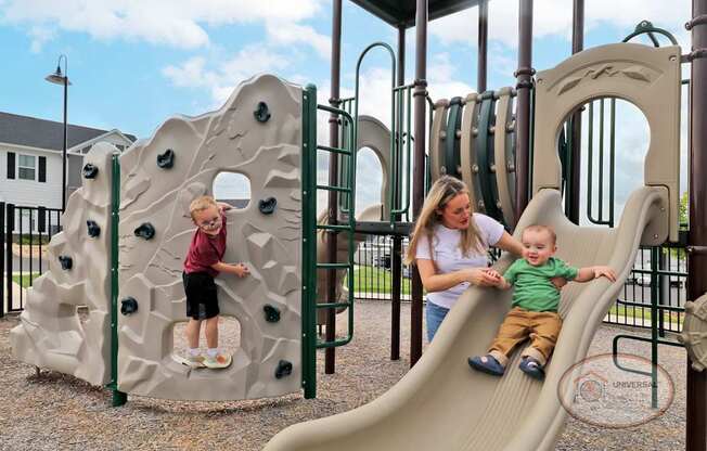 A mother and two children playing on a slide on a playground.