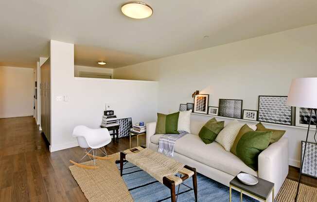 Living room wit partial wall into bedroom area. Hallway visible with build-in storage. Staged with a couch, coffee table, rug and chair.at 19th & Mercer, Seattle Washington