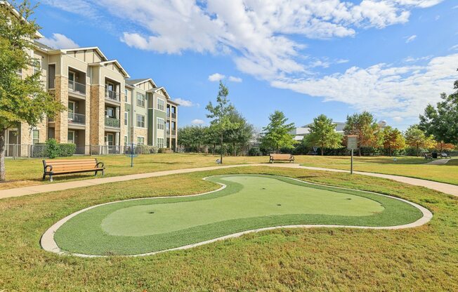 A park with a green lawn and apartment buildings in the background.