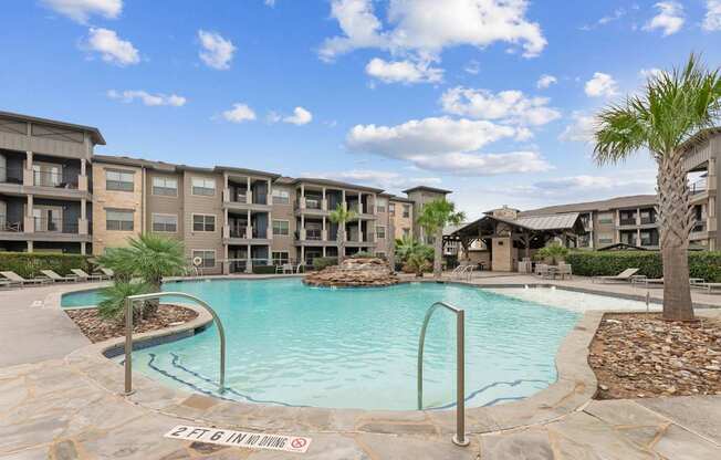 A swimming pool surrounded by apartment buildings and palm trees.