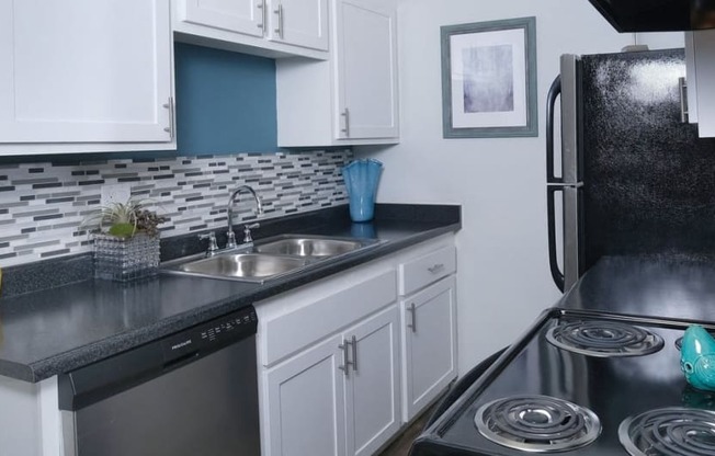 Fifteen 50 - Kitchen in Las Vegas apartment near strip with black and silver appliances, tile backsplash, and colorful modern vases on counters