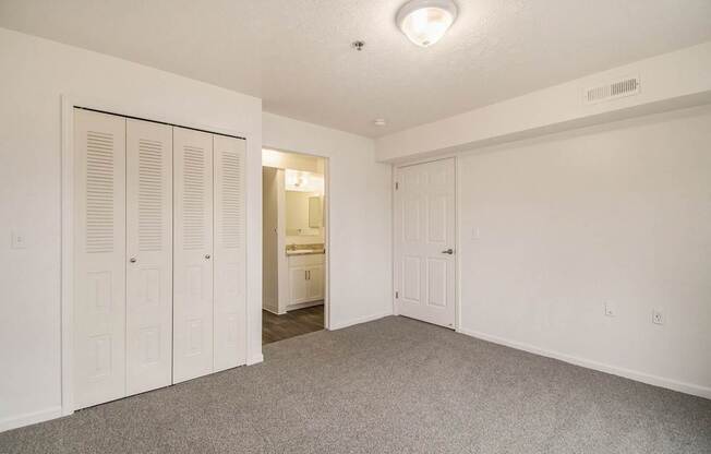A bedroom with a carpeted floor and a door to a walk in closet and a bathroom at West Hampton Park Apartments in Elkhorn, NE 68022