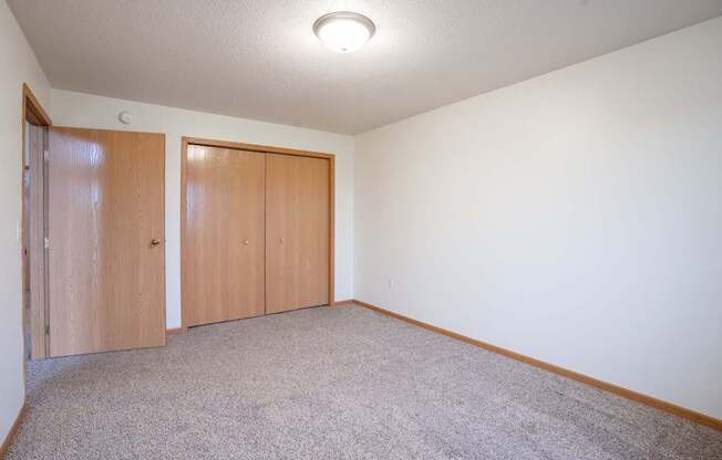A room with two brown doors and a carpeted floor. Fargo, ND Summit Point Apartments