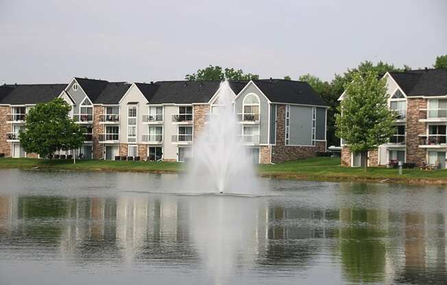 a fountain in the middle of a lake with apartments in the background