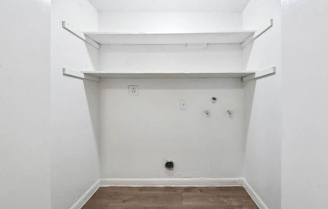 A white wall with a shelf and a brown floor.