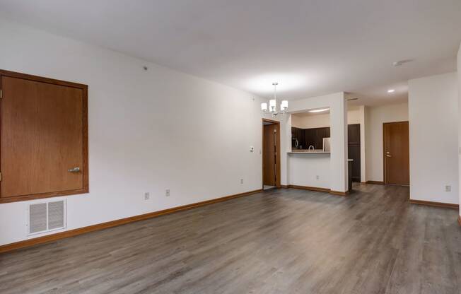 an empty living room with wood floors and white walls and a kitchen