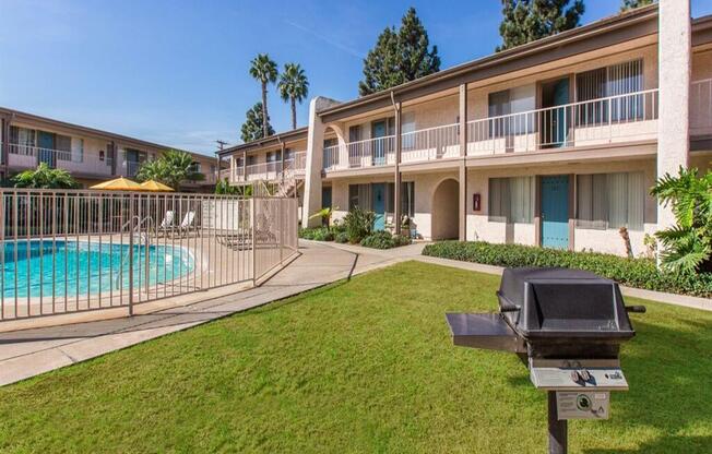 a grassy area with a grill and a pool in the background