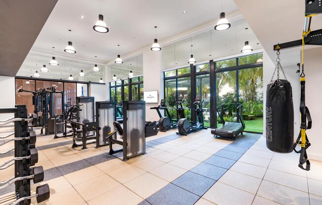 The fitness center at Modera Aventura features floor-to-ceiling glass, modern equipment, and views of the tropical courtyard.
