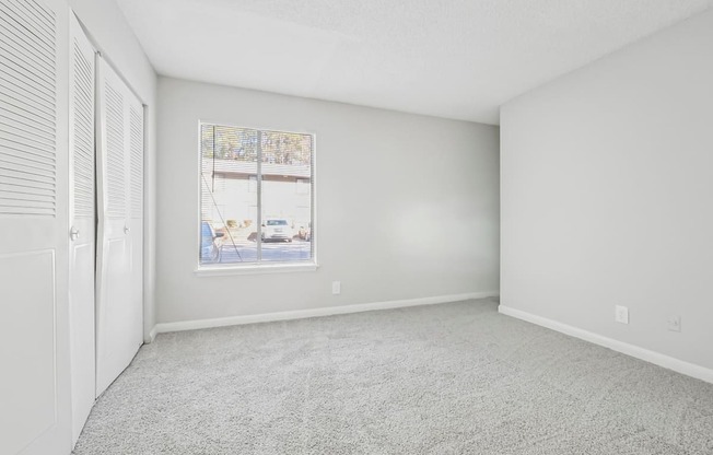 Second bedroom with a carpeted floor and a large window in B1 floor plan at Riverwood Crossing apartments in Roswell, GA.