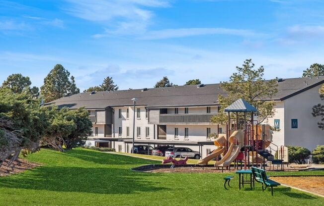 a playground in front of an apartment building with a large yard