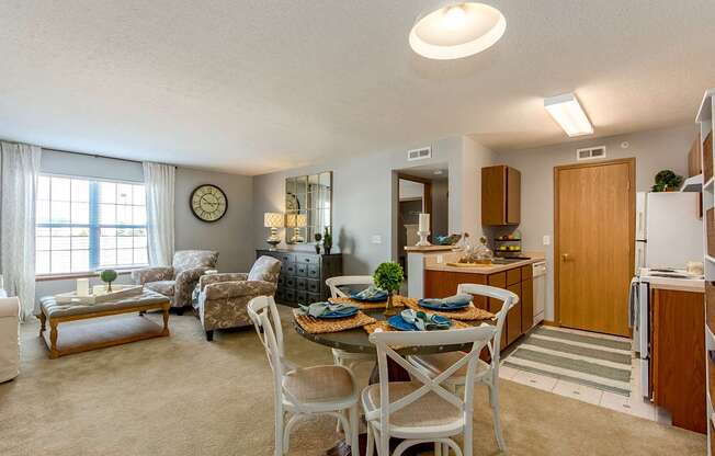 A well-lit, clean, and organized living room with a dining area and kitchen in the background.