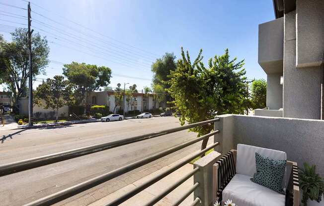 A white chair with a green pillow is on a balcony overlooking a street.