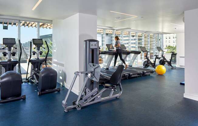 A gym with a row of treadmills and a woman working out.