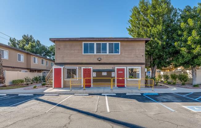 a small brown building with red doors and yellow railing in front of a parking lot